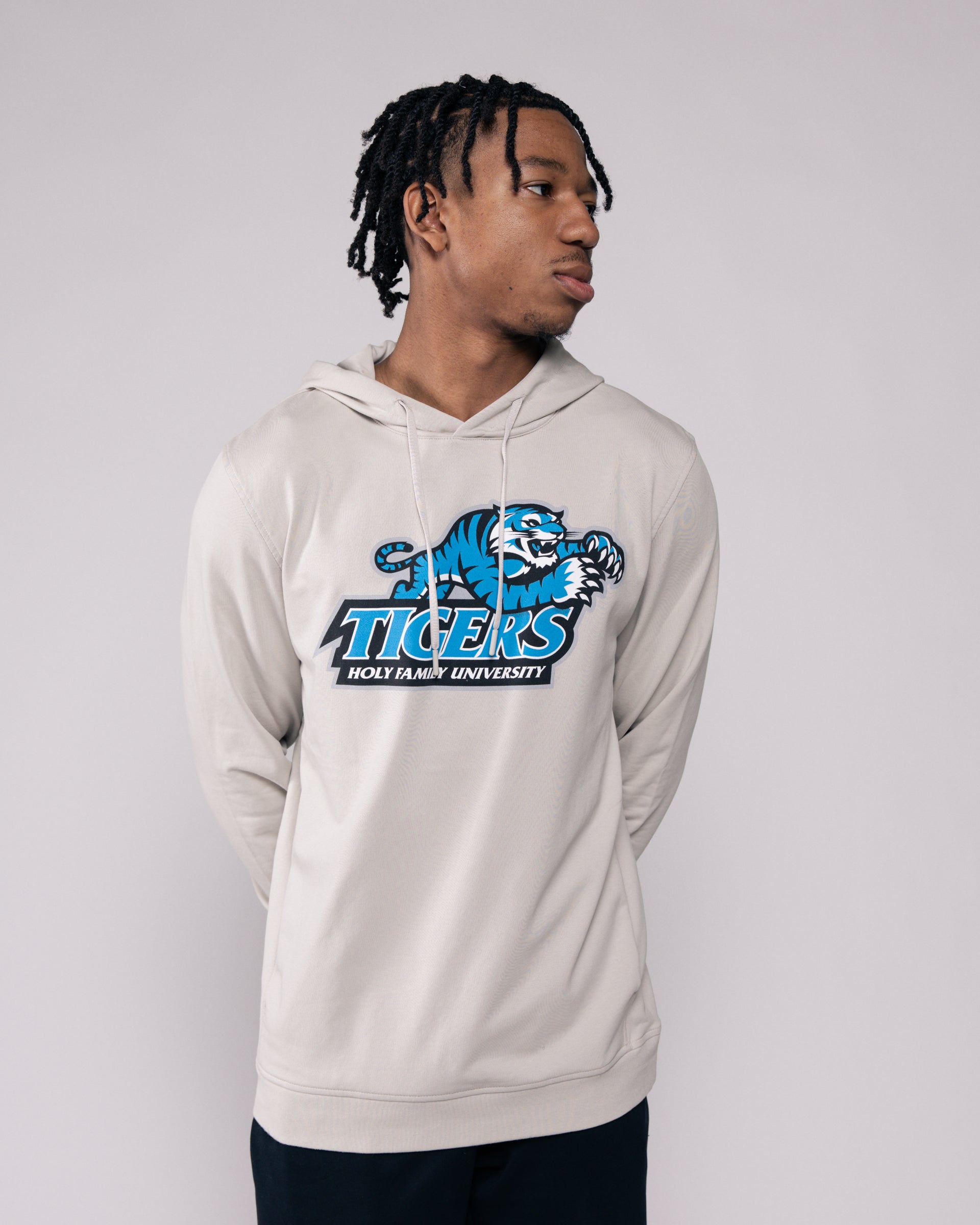 Person wearing a beige hoodie with a blue and white tiger logo on a plain background