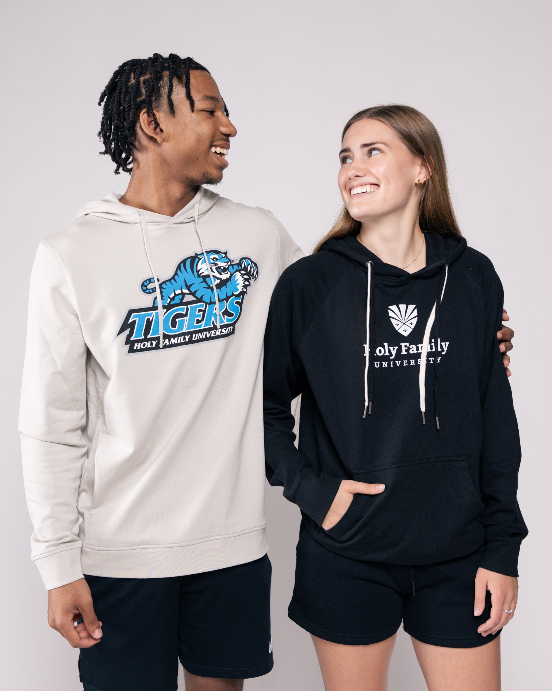 Two people wearing branded hoodies with 'Tigers' and 'Holy Family University' logos.